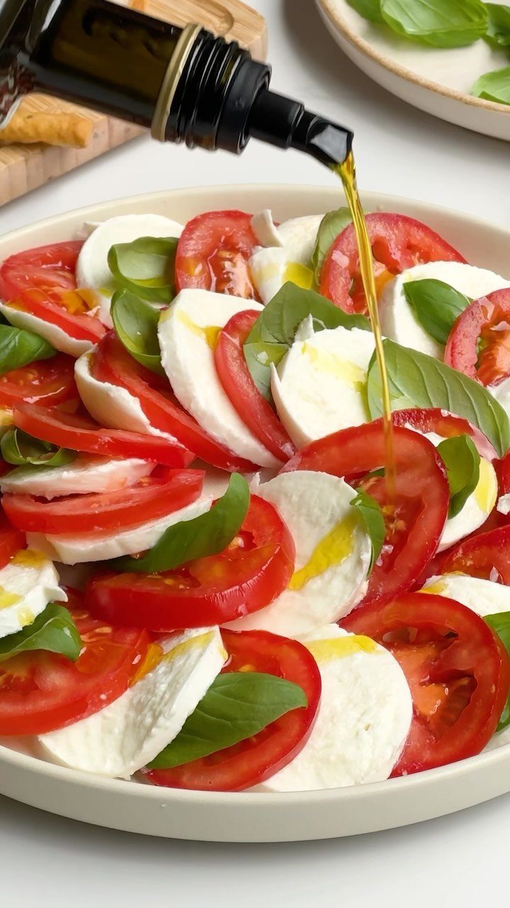 Caprese salad with sliced tomatoes, mozzarella, and basil leaves with olive oil pouring.