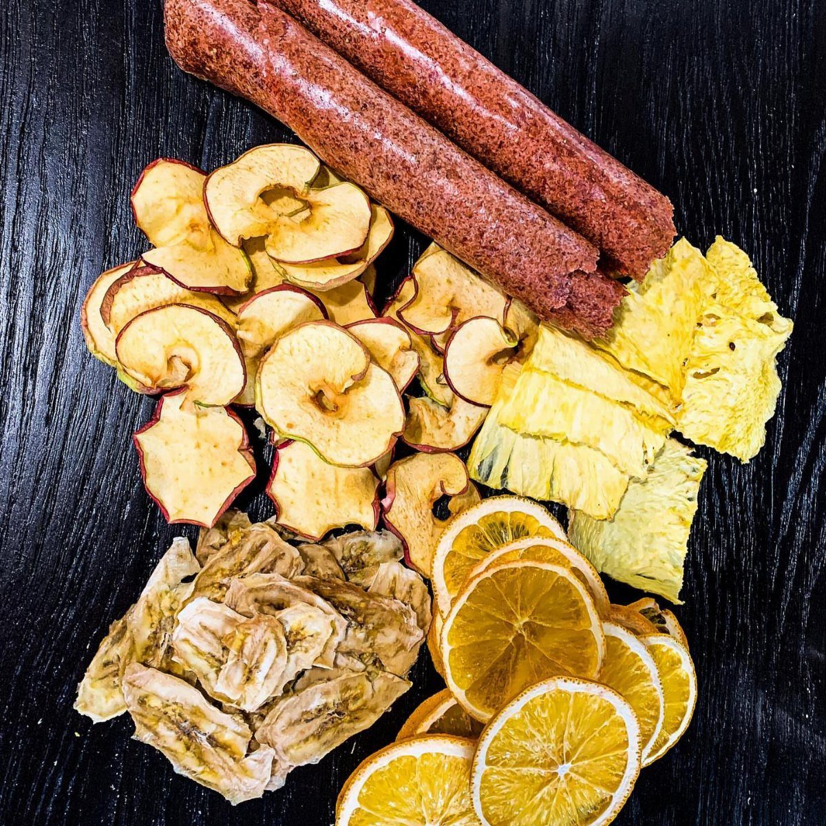 Dried apple, banana, and orange slices with meat sticks on a dark background.