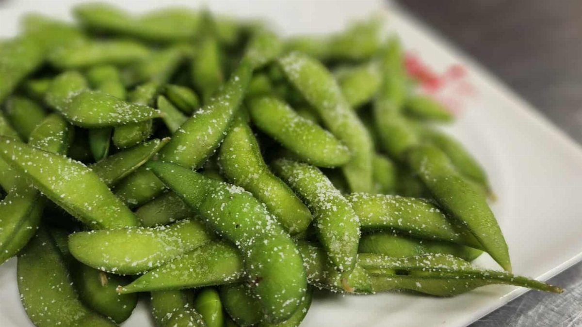 Green edamame pods sprinkled with salt on a white rectangular plate.