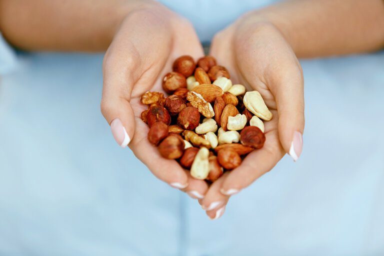 Mixed nuts held in two cupped hands against a soft blue background.
