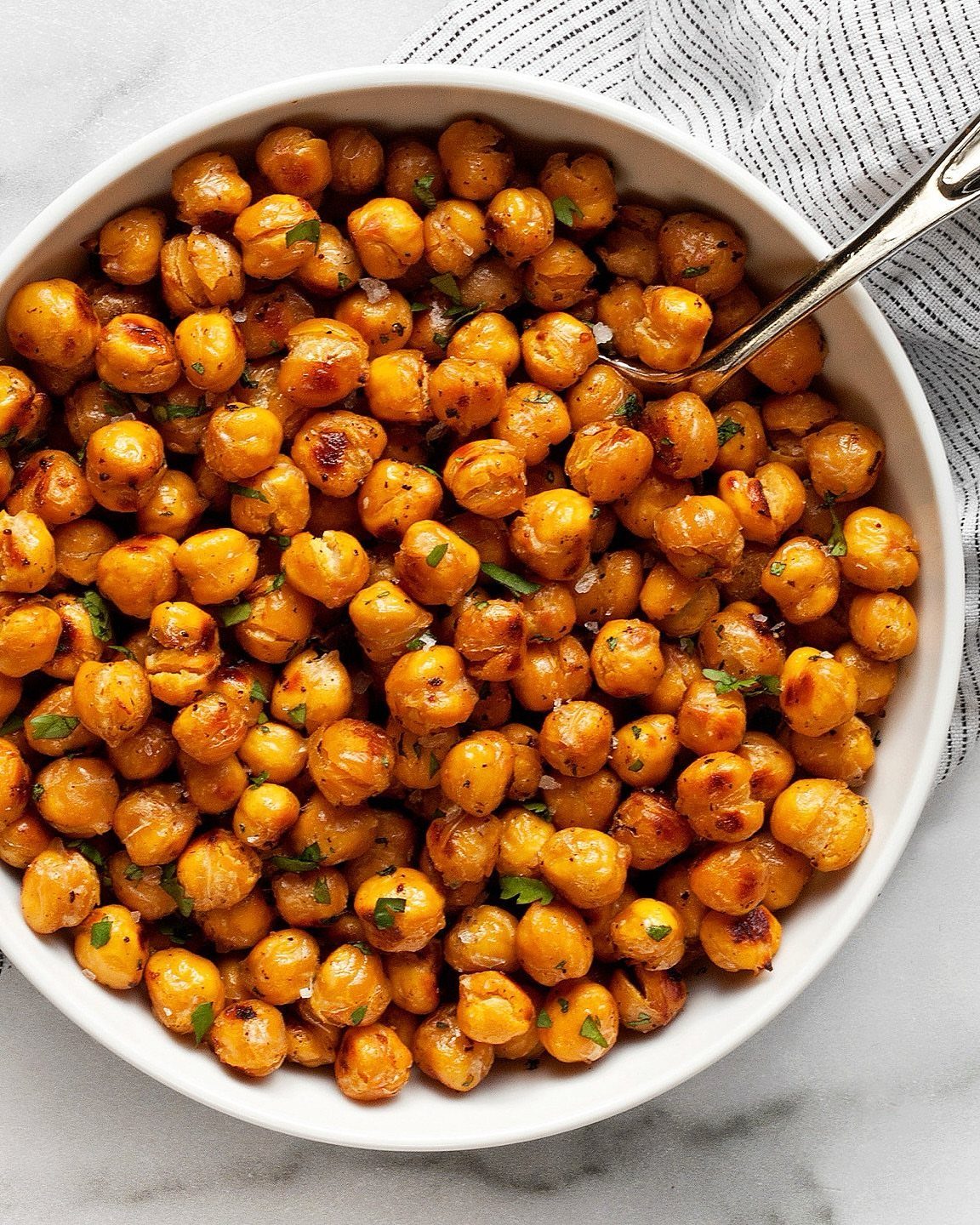 Roasted chickpeas with herbs in a white bowl on a marble surface