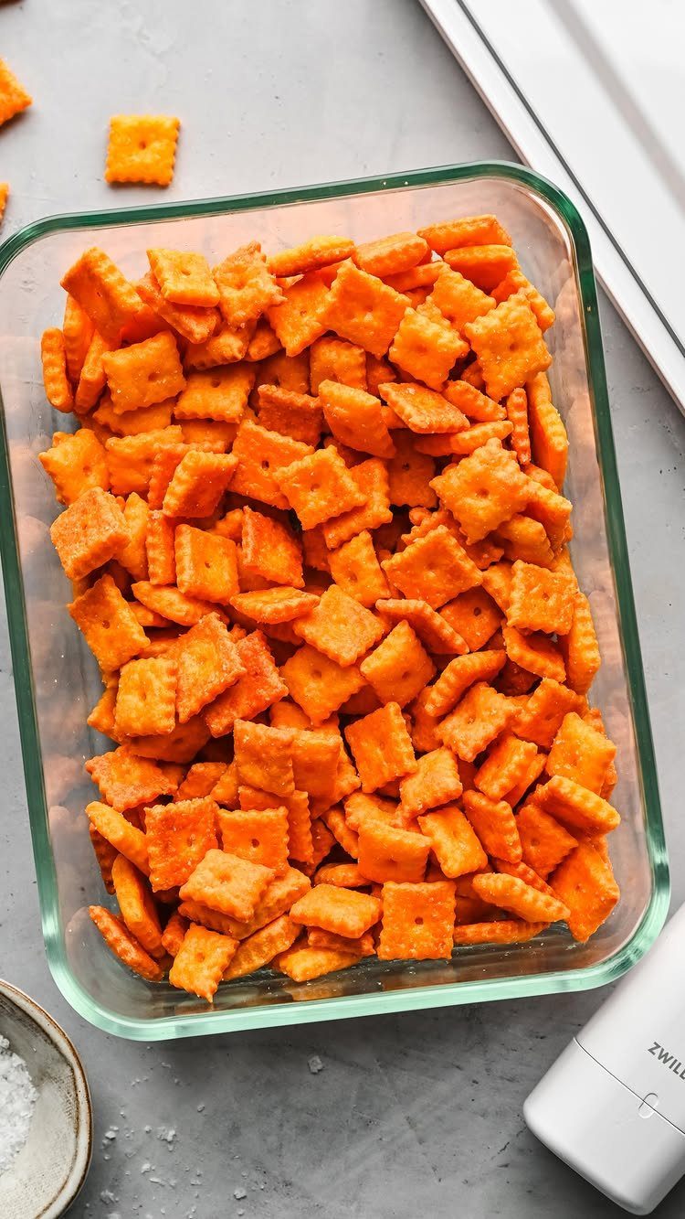 Orange seasoned square crackers filling a clear glass baking dish on grey stone.