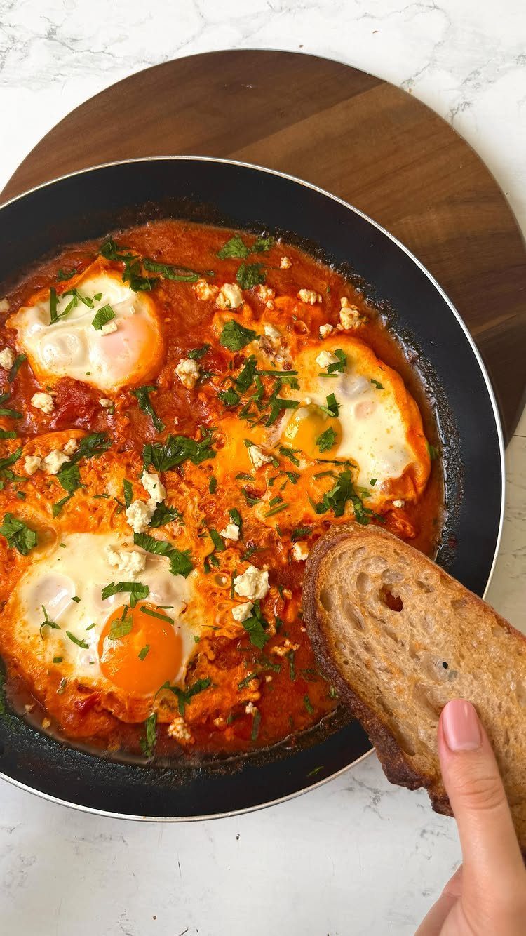 Shakshuka with poached eggs and feta in a pan with toasted brown bread.