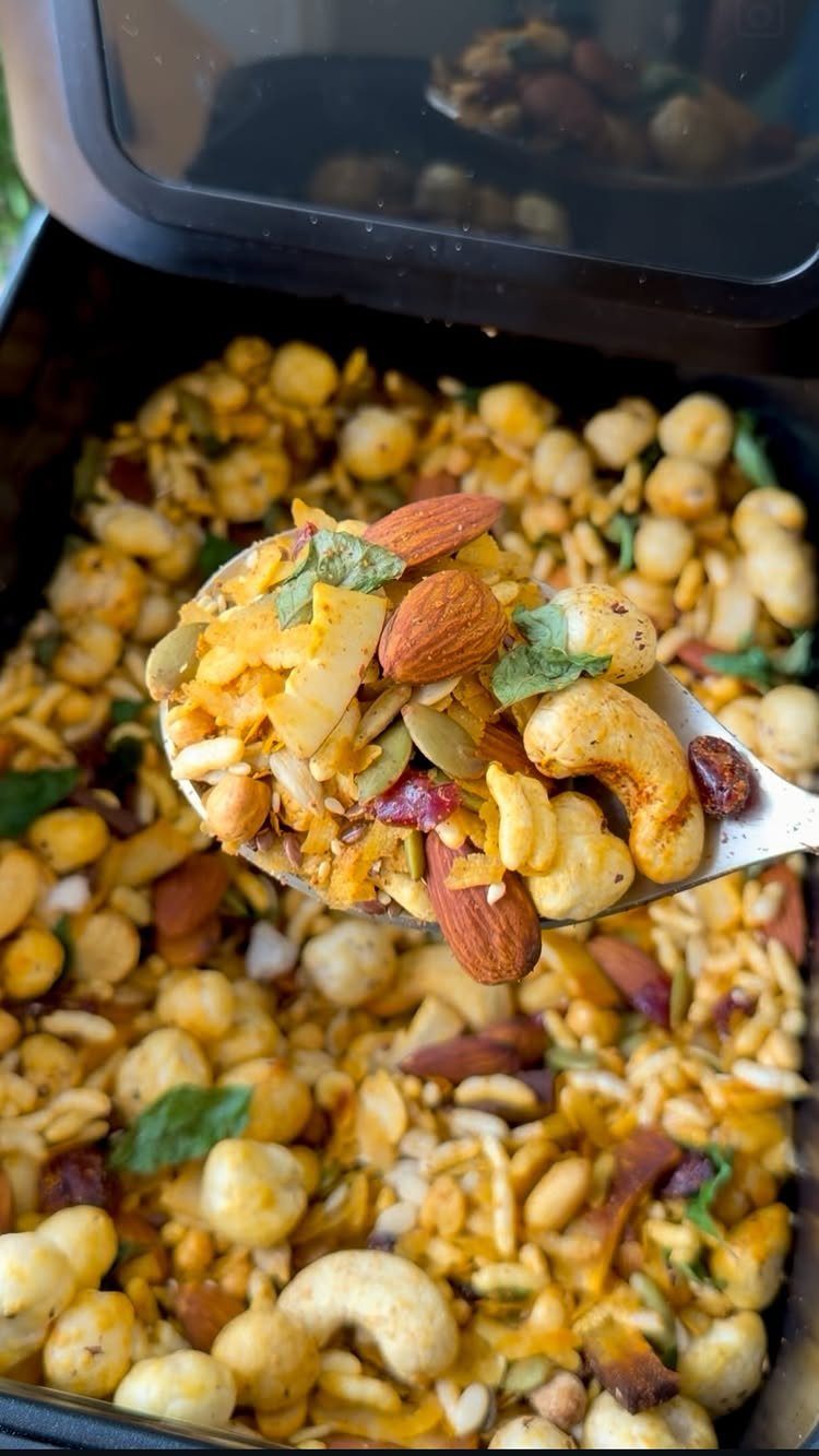 Spoon lifting a savory trail mix with almonds, cashews, and chickpeas from a container.