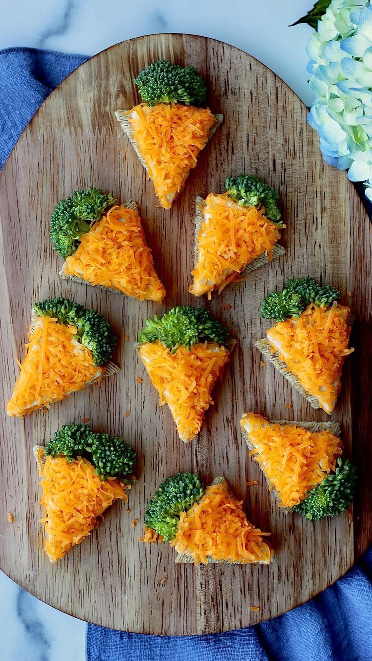 Whole-grain crackers topped with shredded cheddar cheese and broccoli on a wooden board.