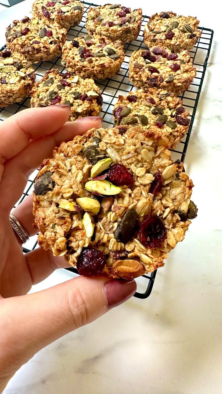 Oatmeal cookie with dried cranberries and pumpkin seeds held over a cooling rack.