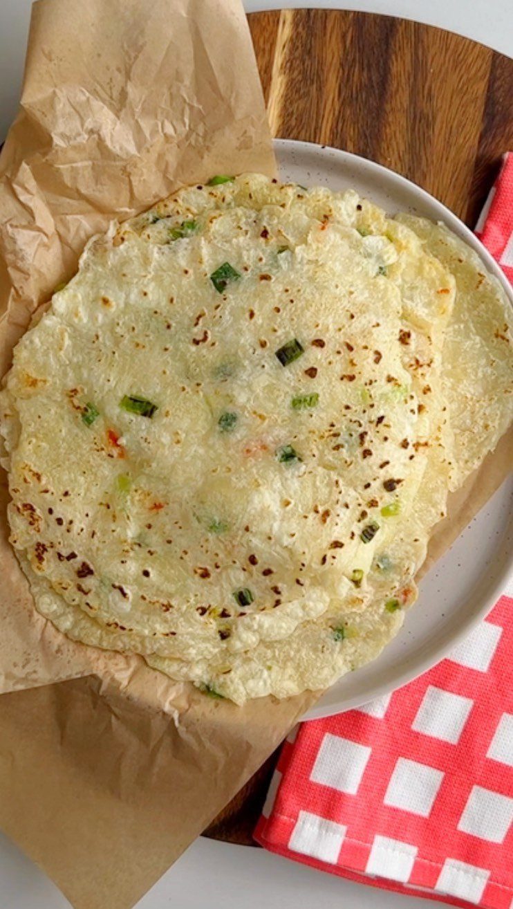 Stack of homemade cassava flour tortillas with green onions on a white plate.