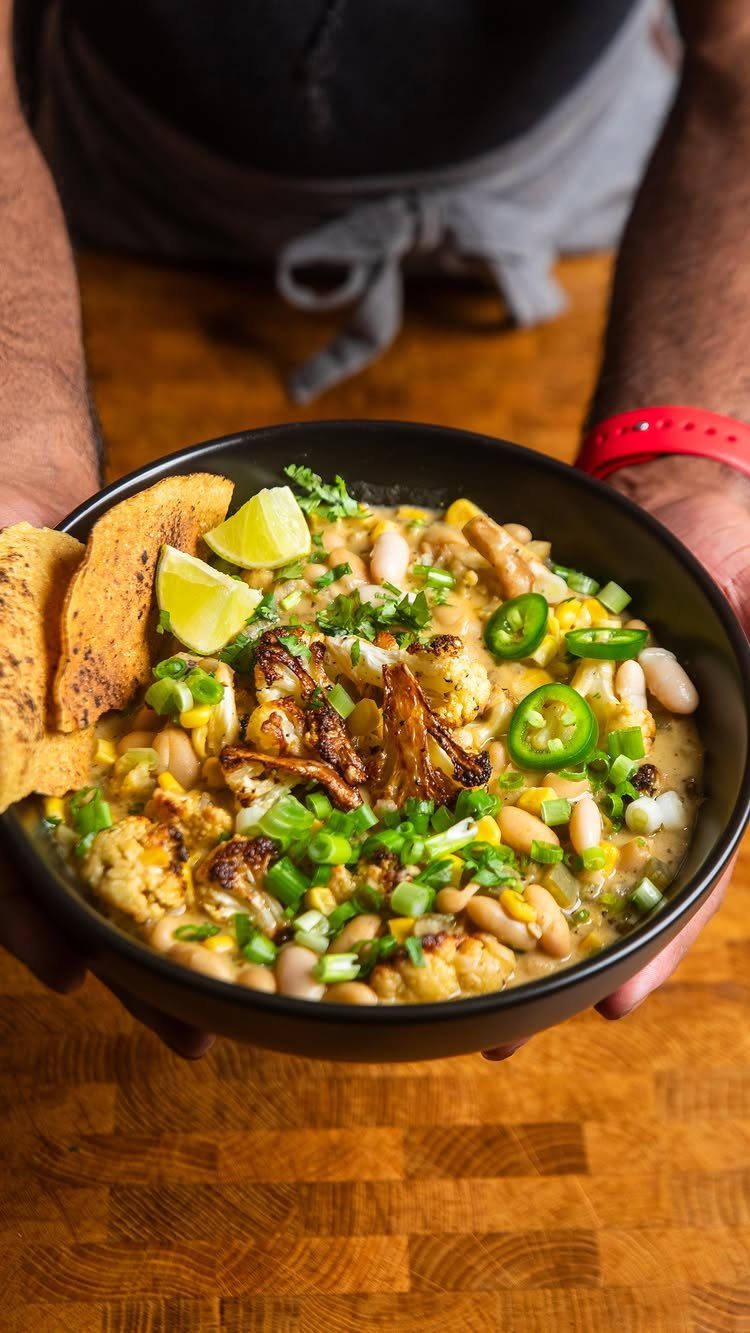 Creamy cauliflower chili with white beans, corn, and jalapeños in a black bowl.