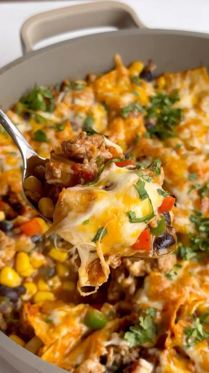 Chicken enchilada skillet with melted cheese, corn, and beans lifted by a spoon
