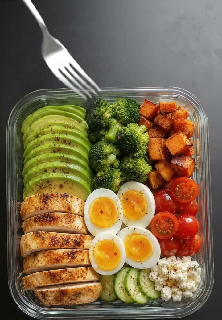 Meal prep container with grilled chicken, boiled eggs, broccoli, sweet potato, and avocado.