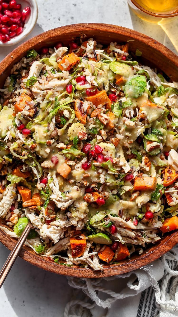 Fall harvest salad with roasted squash, pomegranate seeds, and chicken in a wooden bowl.