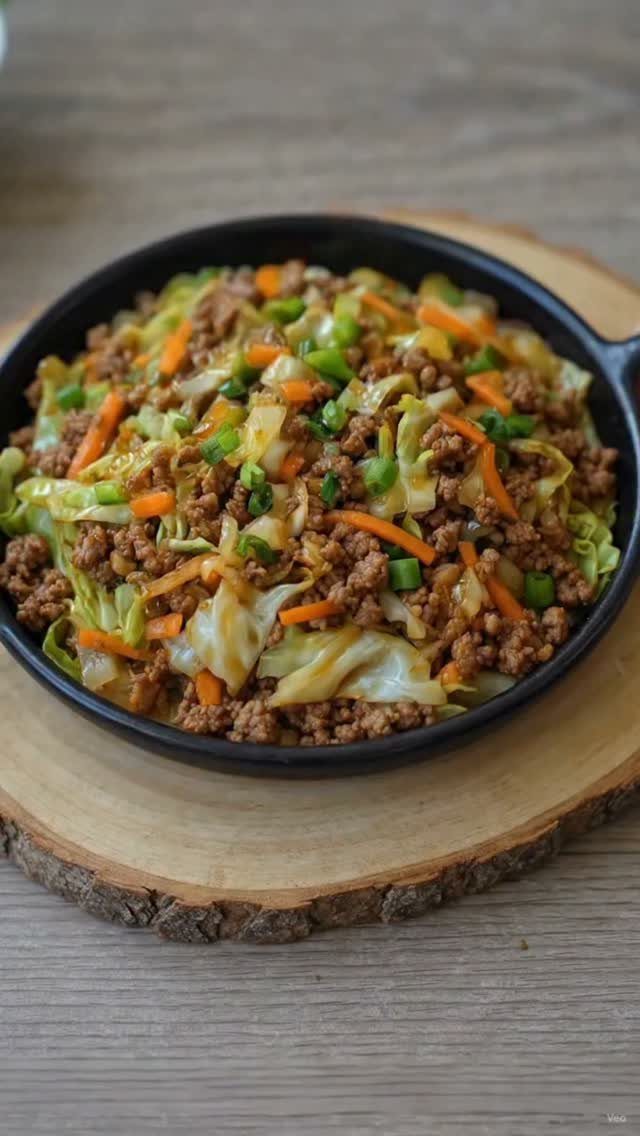 Ground beef and cabbage stir-fry with carrots in a black skillet on wood.