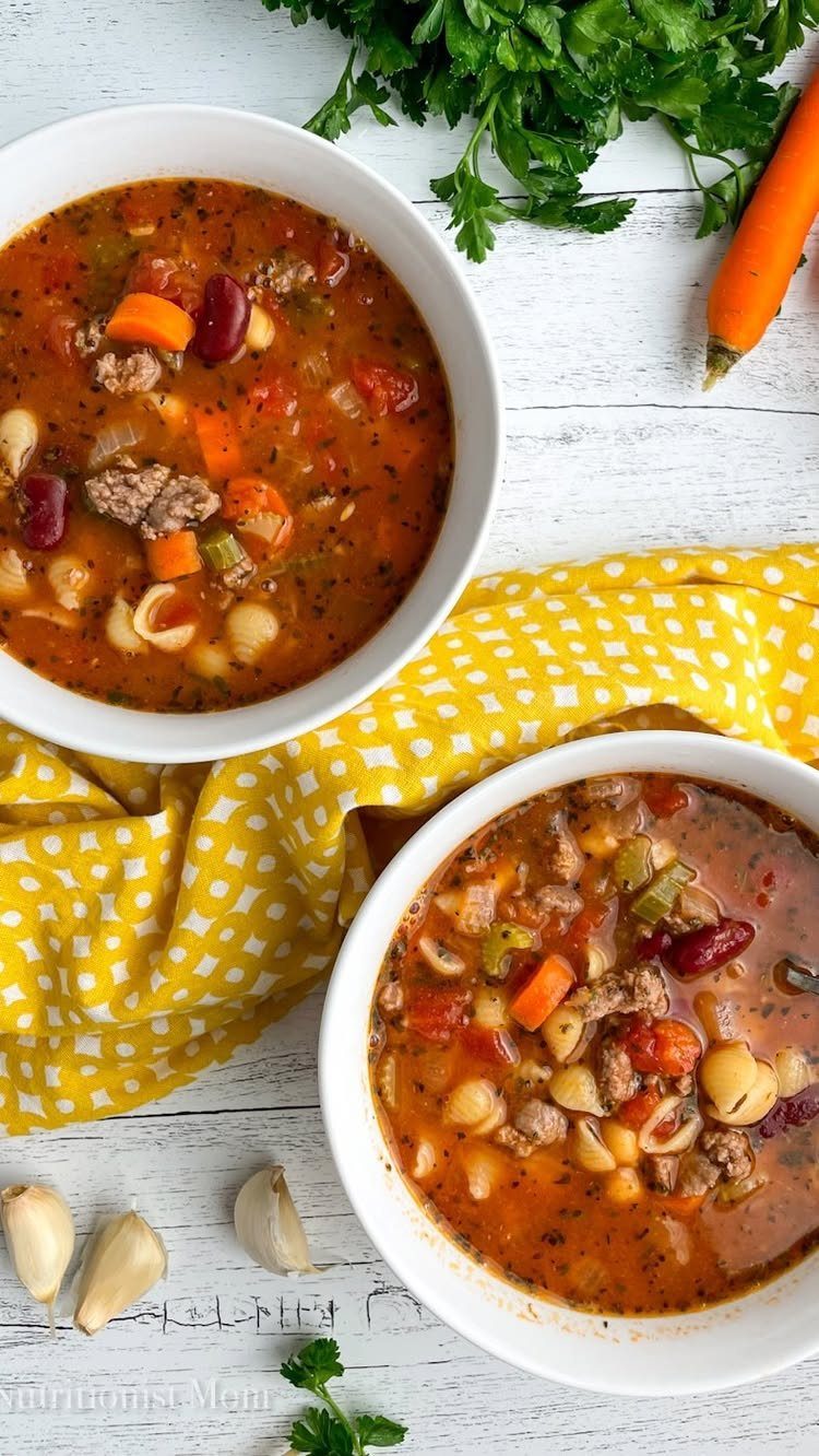 Two bowls of minestrone soup with beans and pasta on a white table.