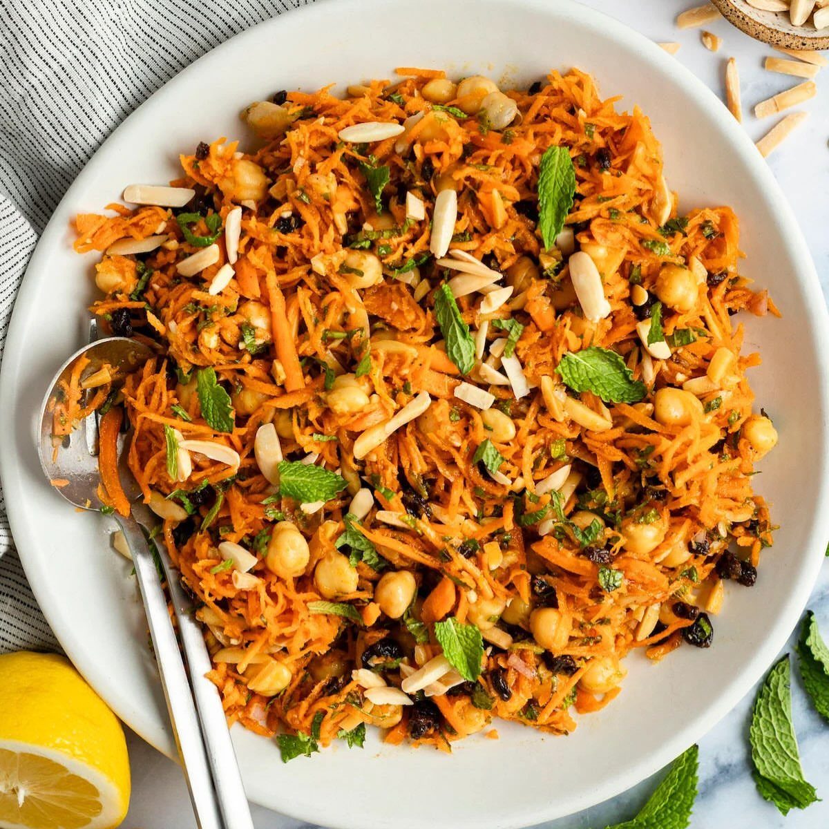 Shredded carrot salad with chickpeas, almonds, and mint in a white bowl.