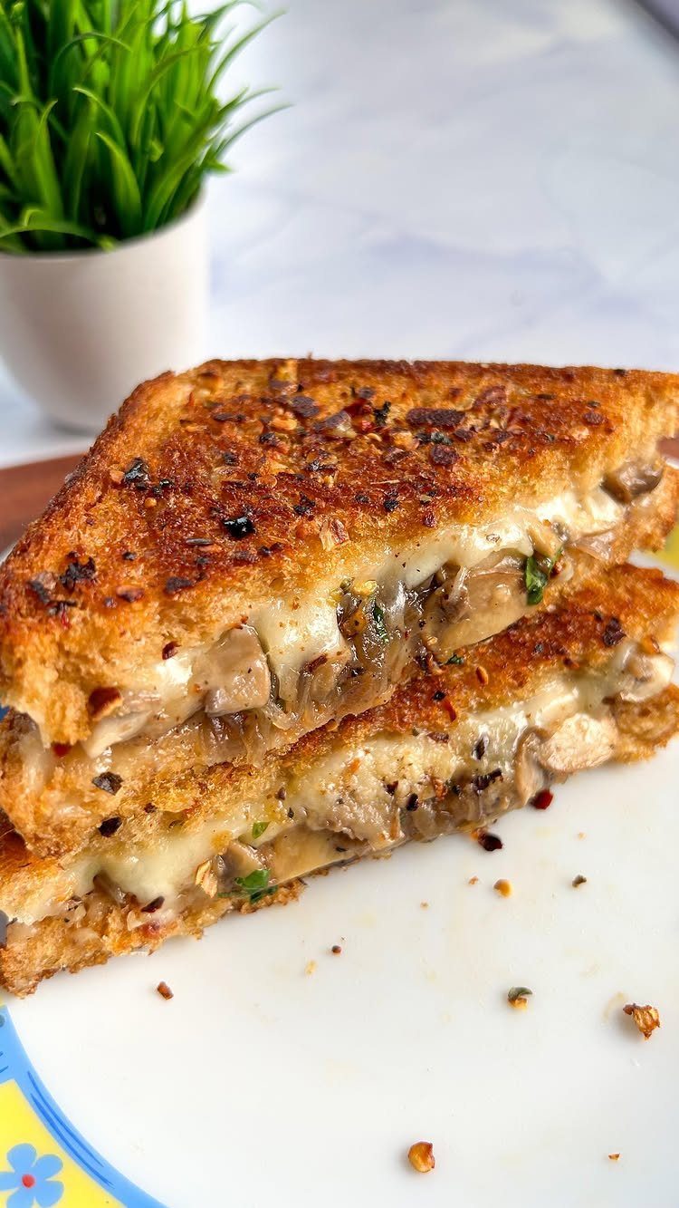 Grilled cheese sandwich with melted cheese and mushrooms on a white plate.