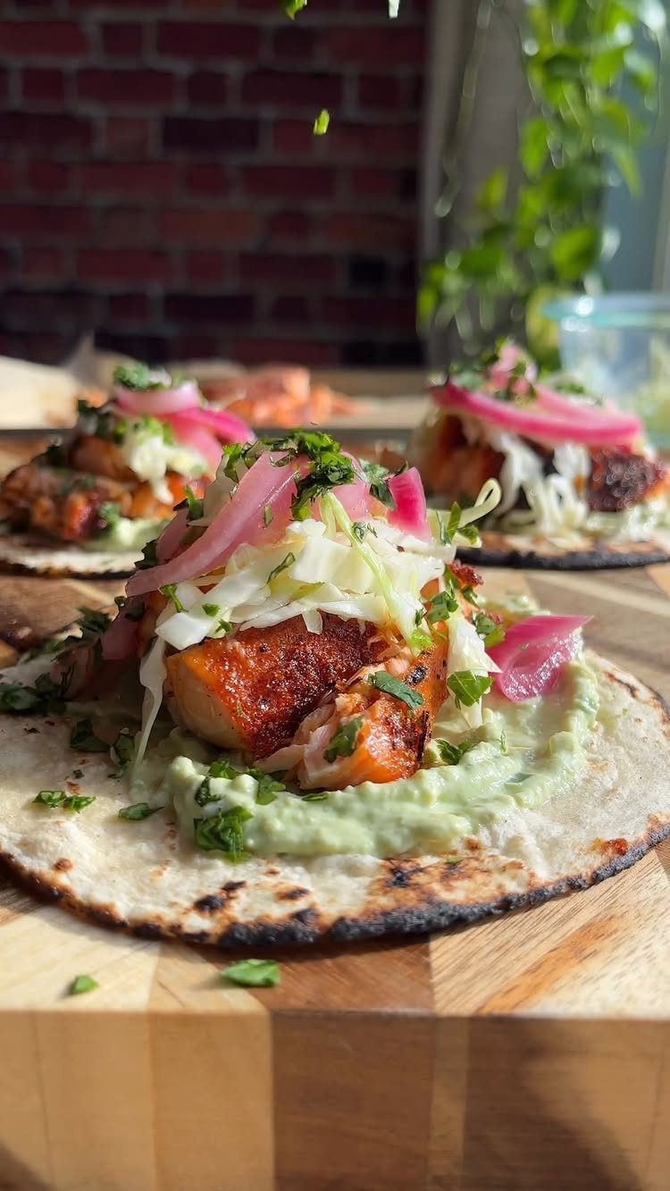 Salmon tacos with cabbage, pickled onions, and guacamole on a wooden board.