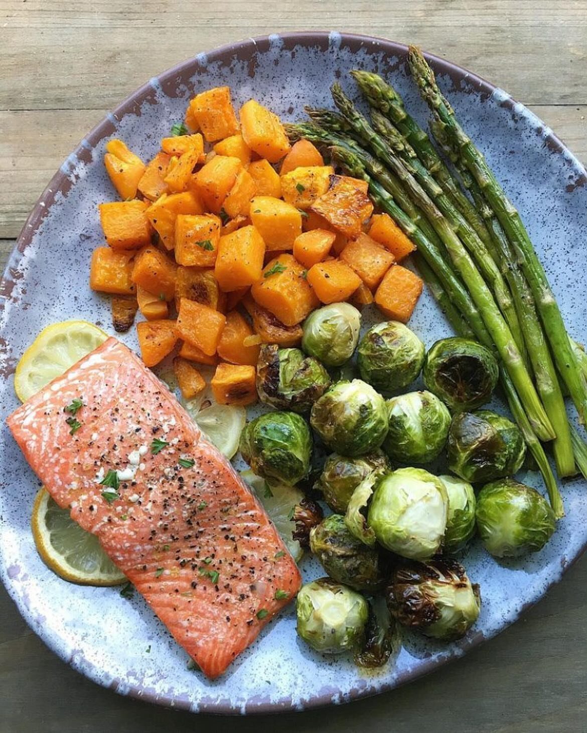 Cooked salmon fillet with lemon, roasted squash, brussels sprouts, and asparagus on a plate.