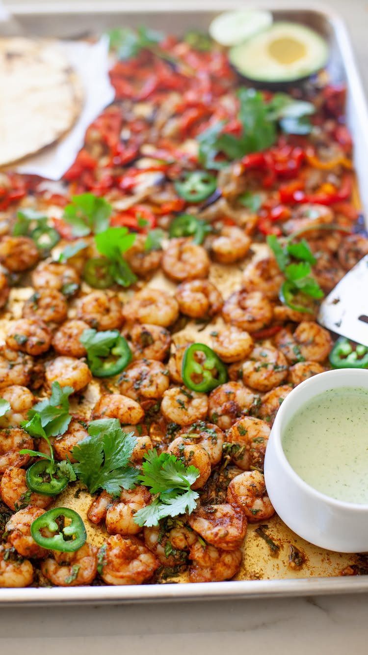 Seasoned shrimp and charred bell peppers on a sheet pan with avocado and sauce.