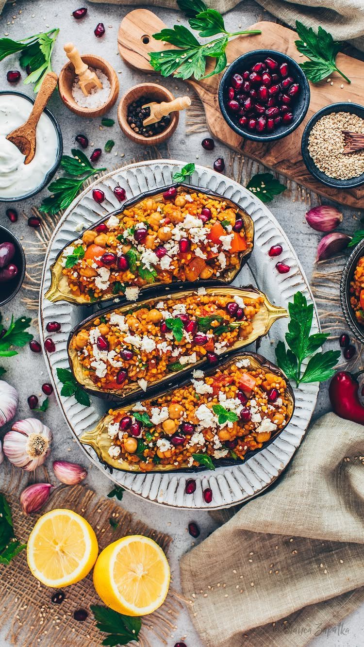 Stuffed eggplant halves with grains and pomegranate seeds on a white platter.