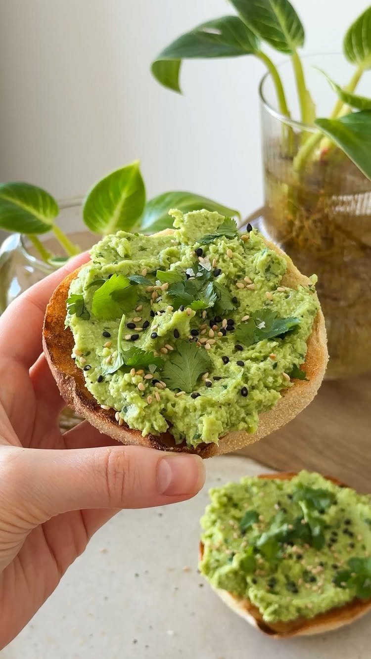 Avocado toast on an English muffin with sesame seeds and cilantro leaves.