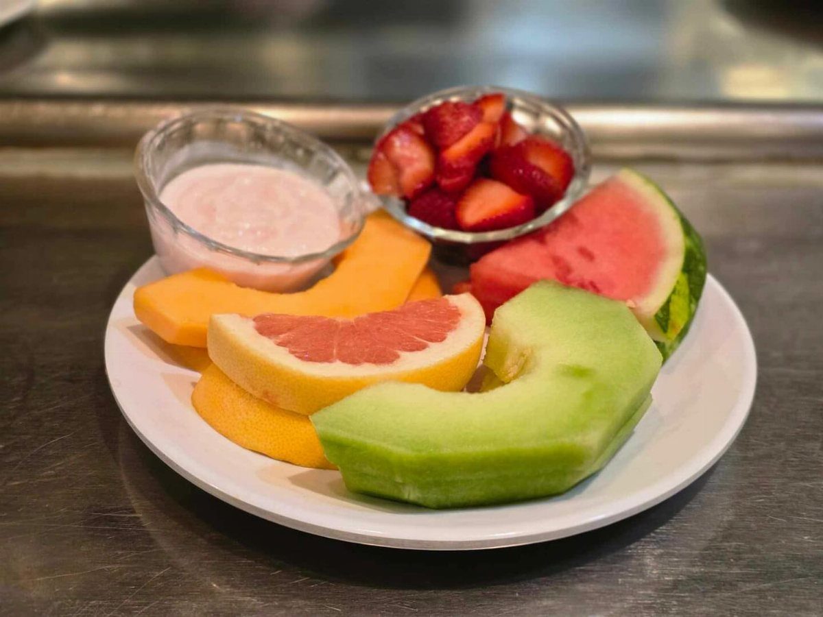 Assorted fresh fruit slices and strawberry dip on a white ceramic plate.