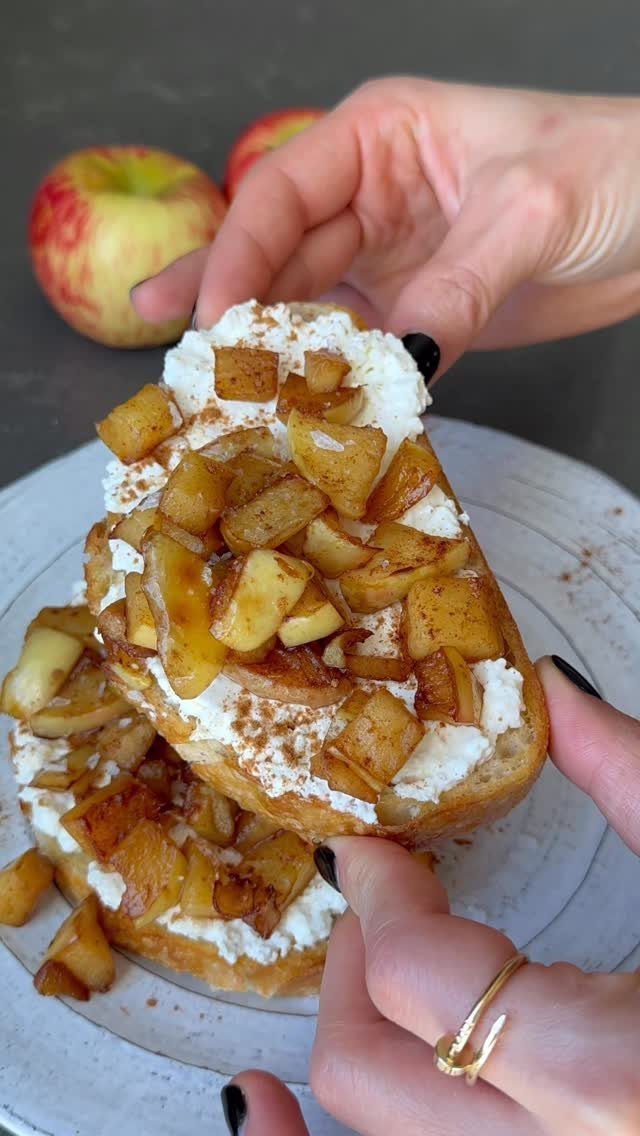 Toasted bread topped with white cream and cinnamon sautéed apple pieces on a plate.