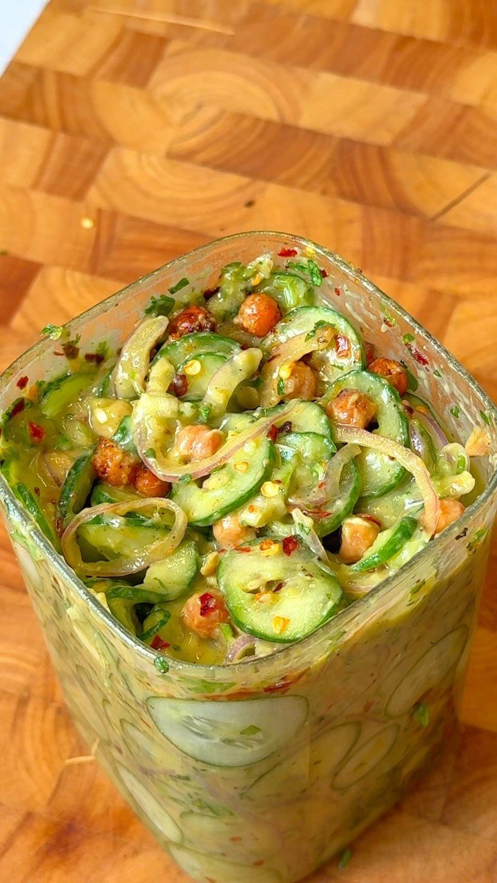 Cucumber and chickpea salad with creamy dressing in a glass jar on wood.