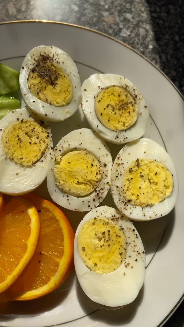 Hard-boiled egg halves with black pepper, orange slices and green vegetables on a plate.