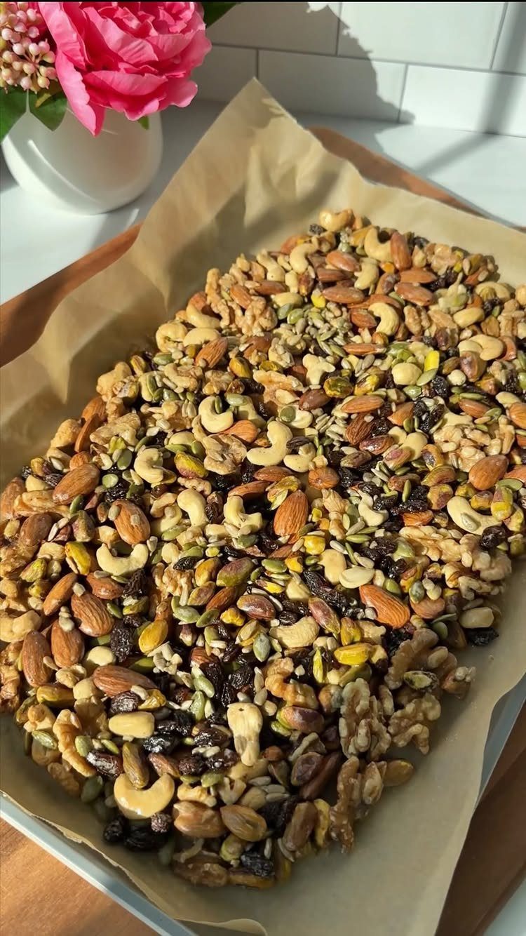 Mixed nuts and dried fruits on parchment paper with a pink rose nearby.
