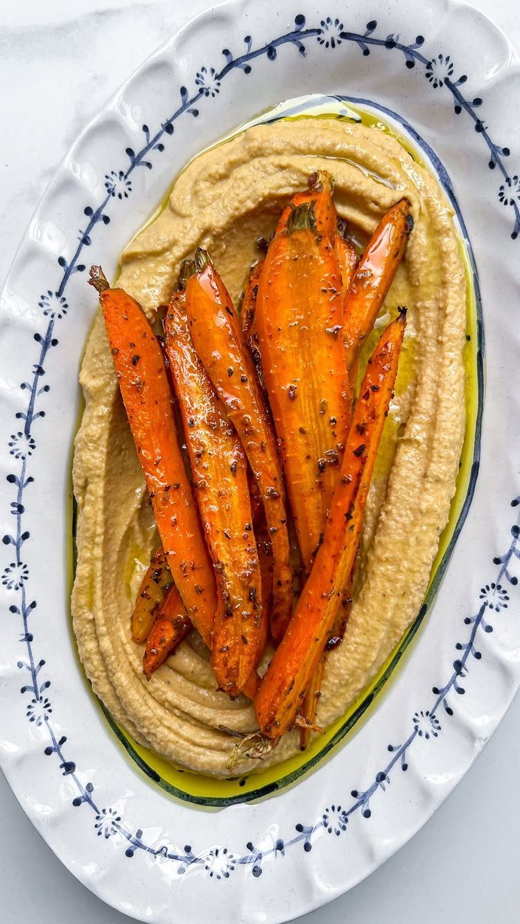 Roasted carrots on a bed of hummus with olive oil on a white platter