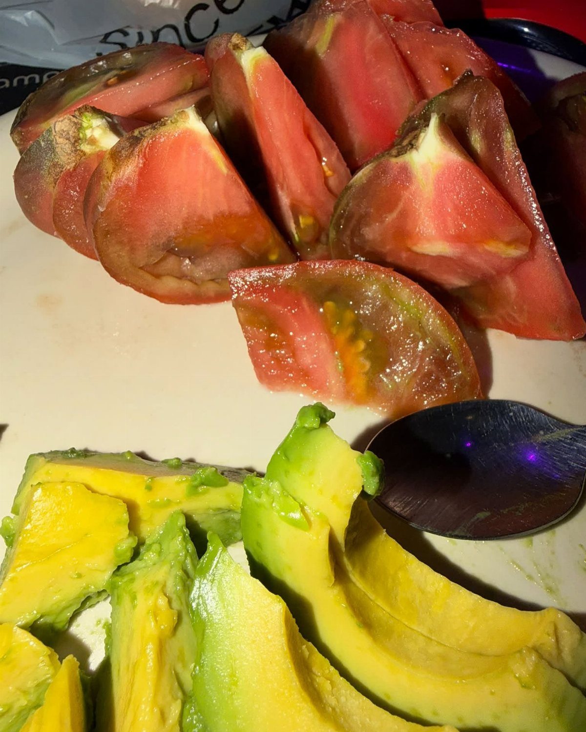 Slices of red tomatoes and green avocado pieces on a white plate.