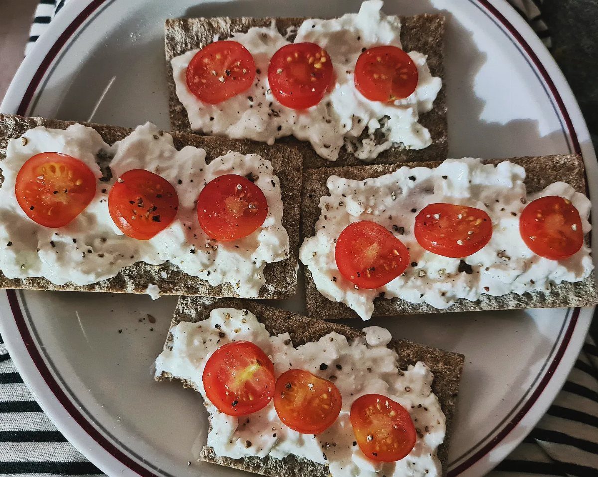 Crispbread crackers topped with white cream cheese and sliced cherry tomatoes on a plate.