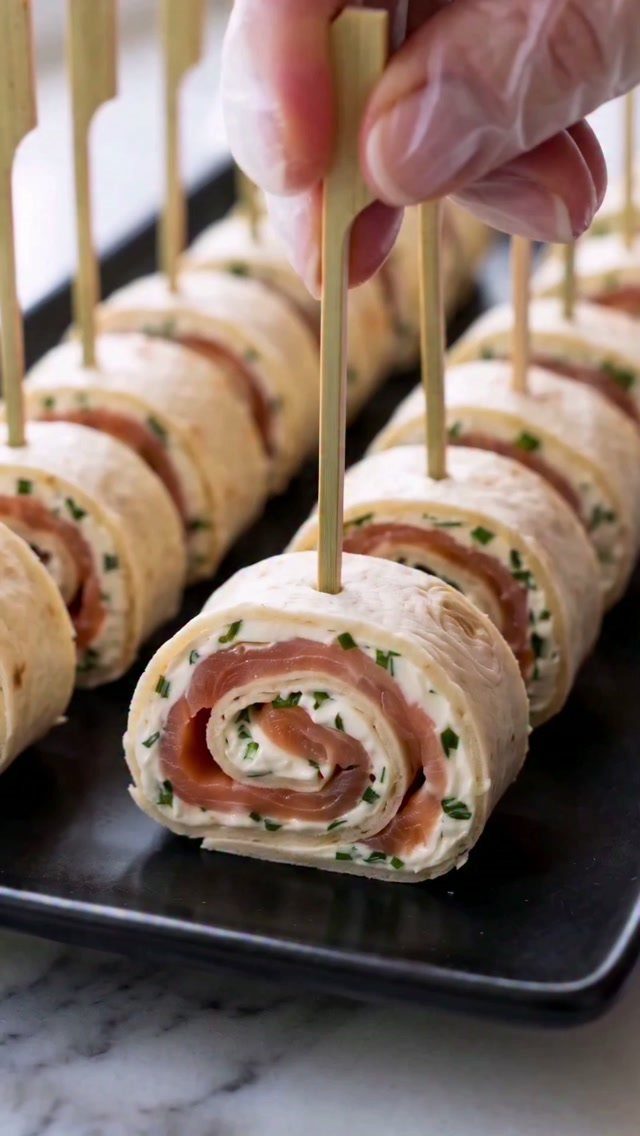 21 Healthy Mini Snacks for Lunchboxes, Parties and Busy Days 11 Smoked salmon and cream cheese pinwheels on a black platter with wooden toothpicks.