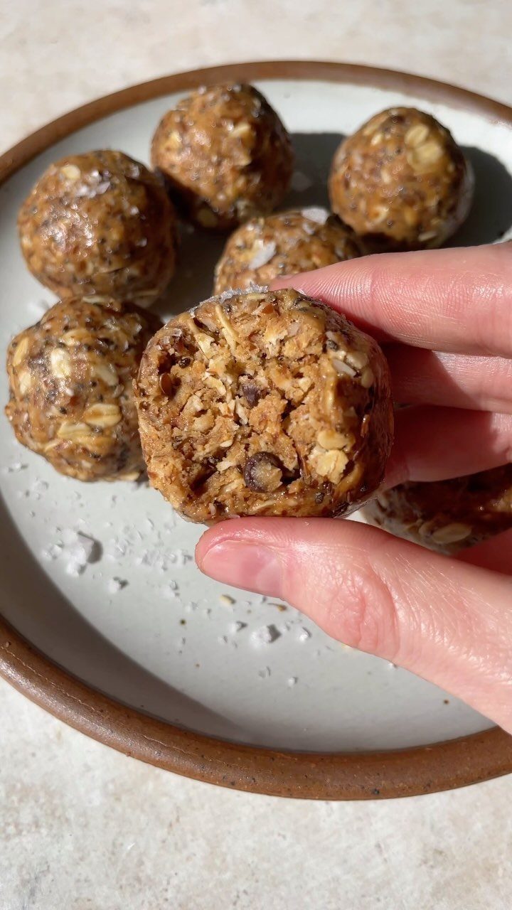 21 Healthy Mini Snacks for Lunchboxes, Parties and Busy Days 6 Hand holding an oat and chocolate chip energy bite over a plate of snacks.