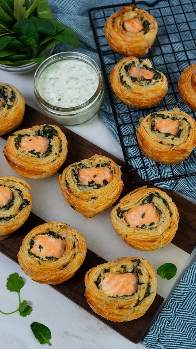 21 Healthy Mini Snacks for Lunchboxes, Parties and Busy Days 19 Salmon and spinach puff pastry swirls on a wooden board with a creamy dip.