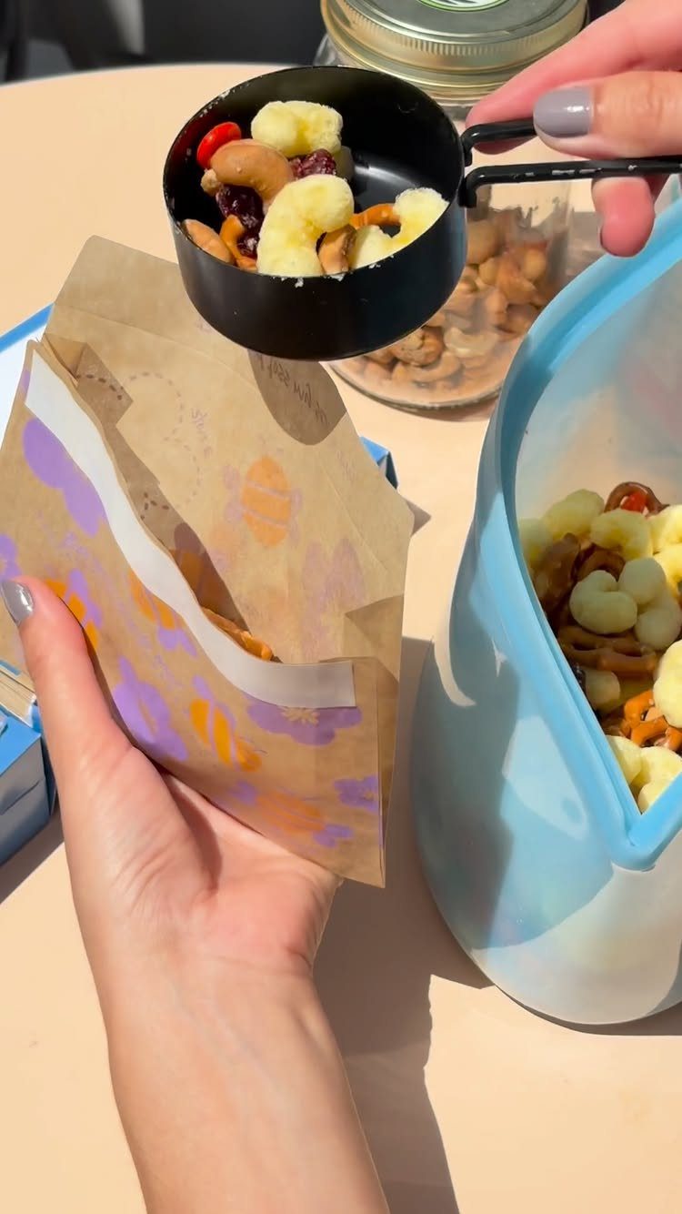 21 Healthy Mini Snacks for Lunchboxes, Parties and Busy Days 8 Trail mix with dried banana and nuts being poured into a paper bag.