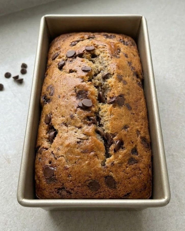 Chocolate chip banana bread loaf inside a metal baking pan on grey surface