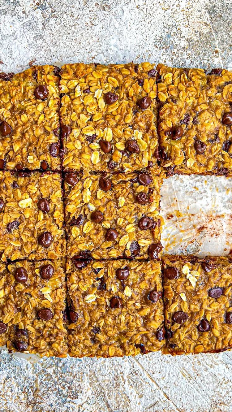Oat bars with chocolate chips arranged in a grid on a stone surface.