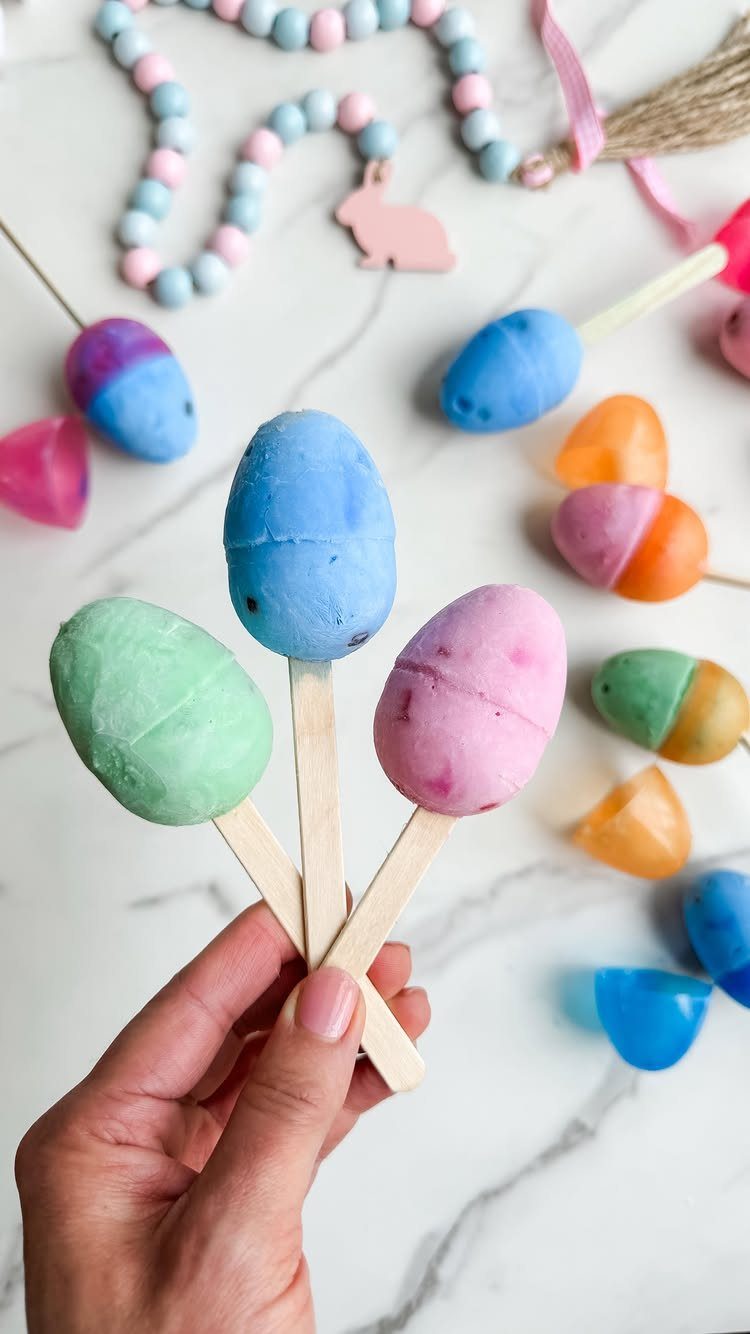 Colorful egg-shaped frozen yogurt pops held by a hand over a marble background.