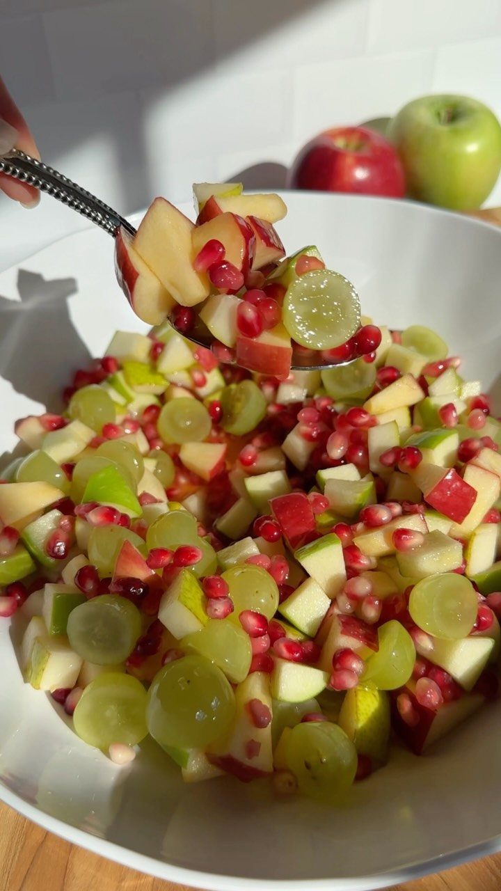 Fruit salad with chopped apples, grapes, and pomegranate seeds in a white bowl.