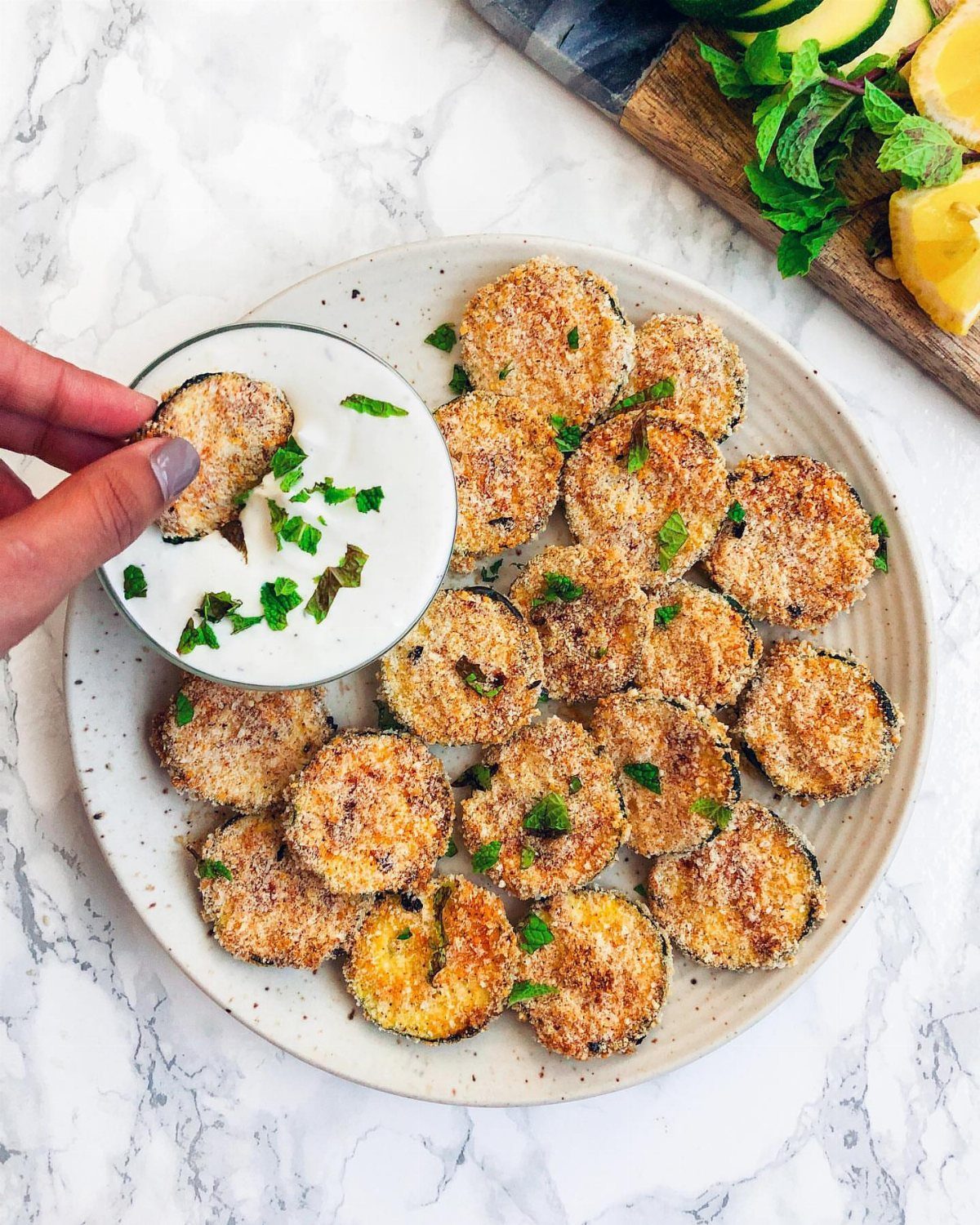Breaded zucchini chips on a white plate with a creamy dipping sauce.