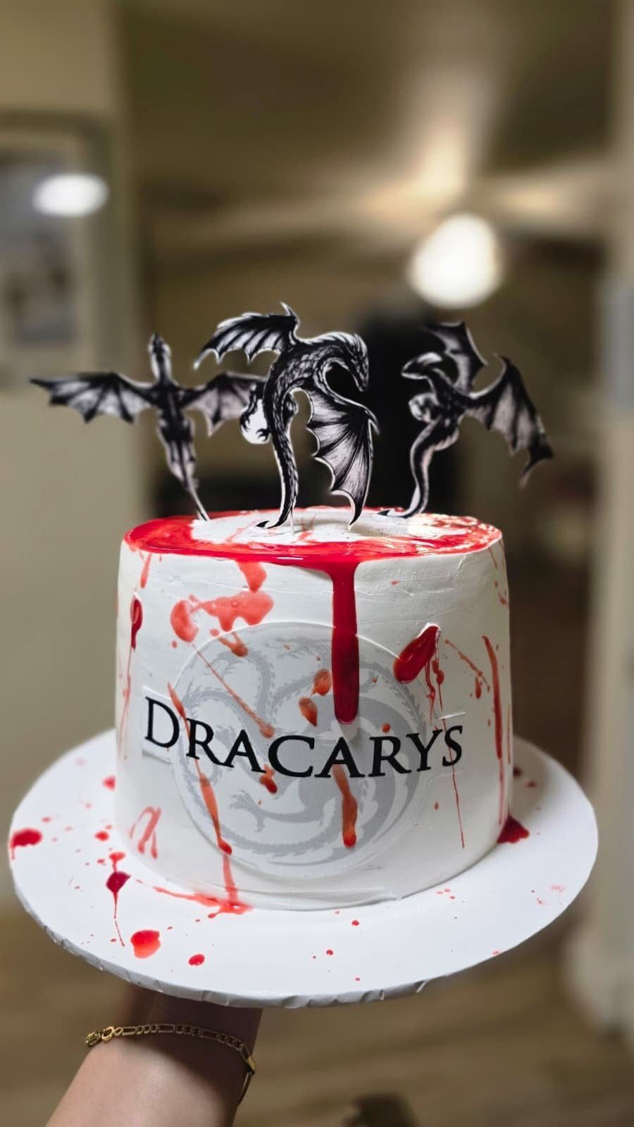 White cake with red icing drips, black dragon toppers, and Dracarys text.
