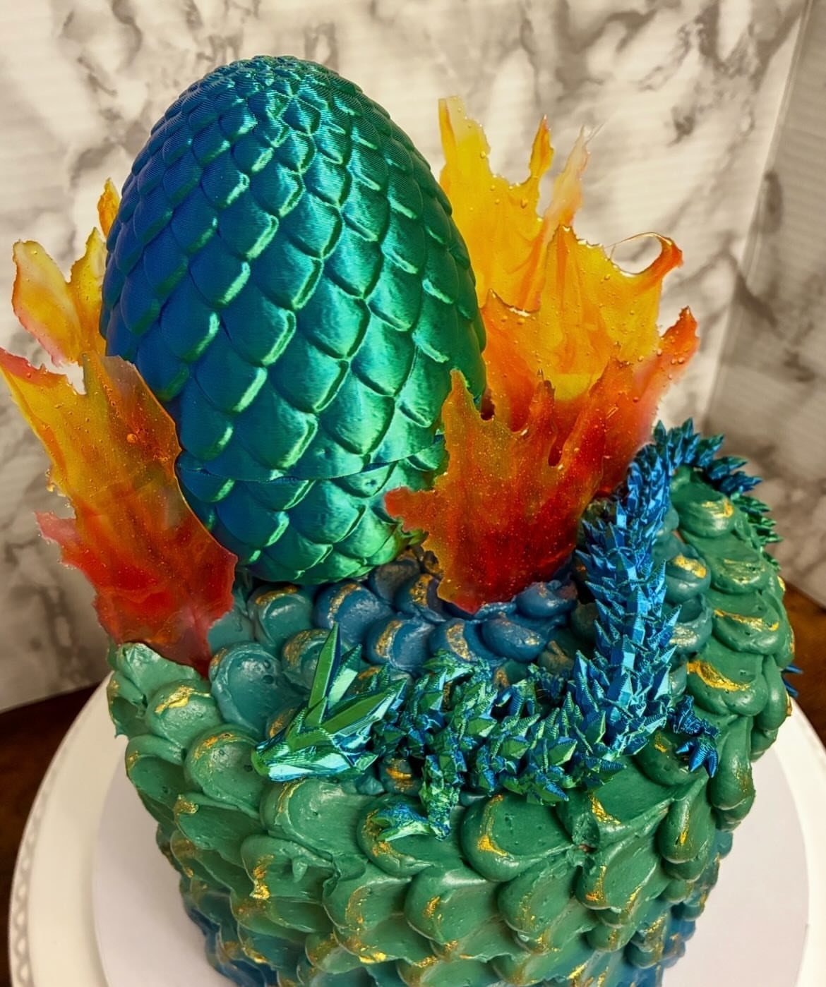 Teal dragon egg cake with a small blue dragon and sugar flames.