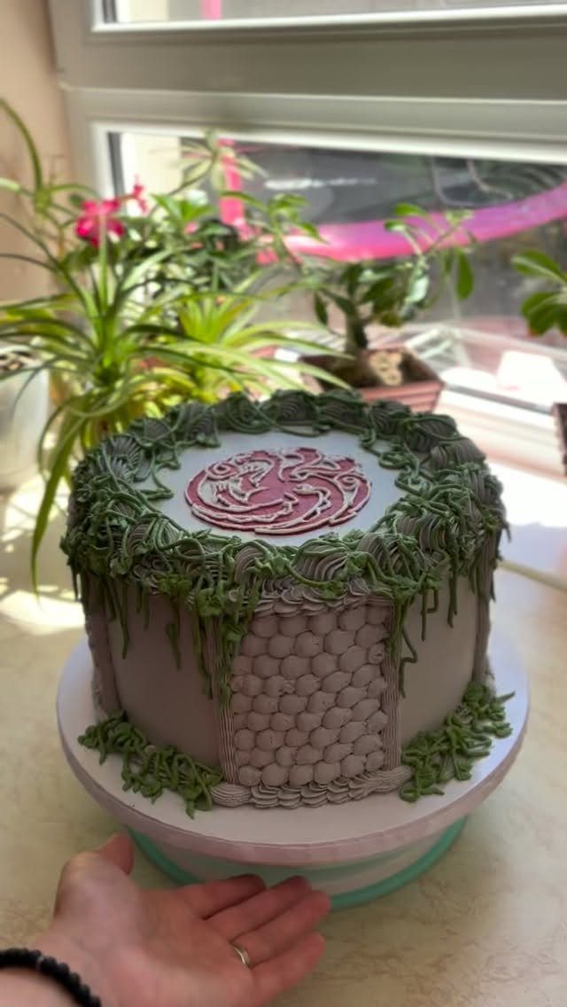 House of the Dragon cake with grey frosting, green vines, and a red dragon emblem.
