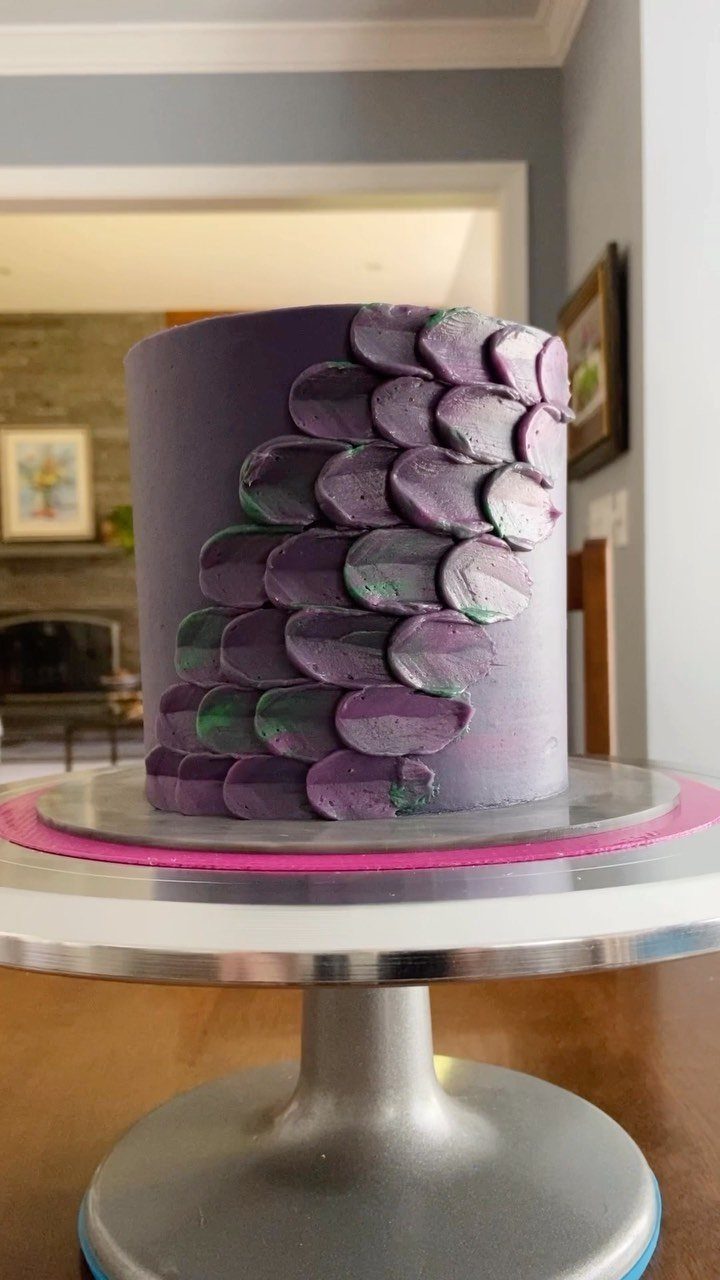 Purple cake with overlapping purple and green buttercream scales on a silver stand.