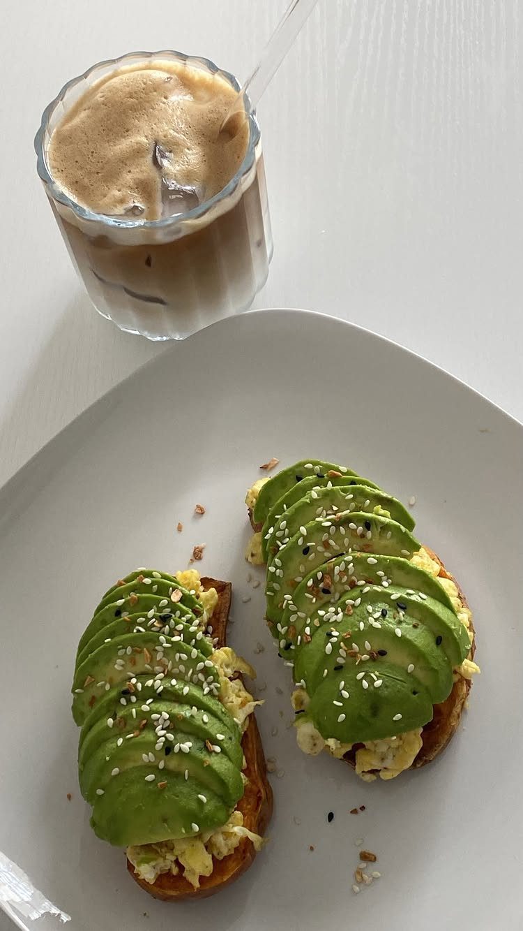 Avocado toast with scrambled eggs and sesame seeds served with iced coffee.