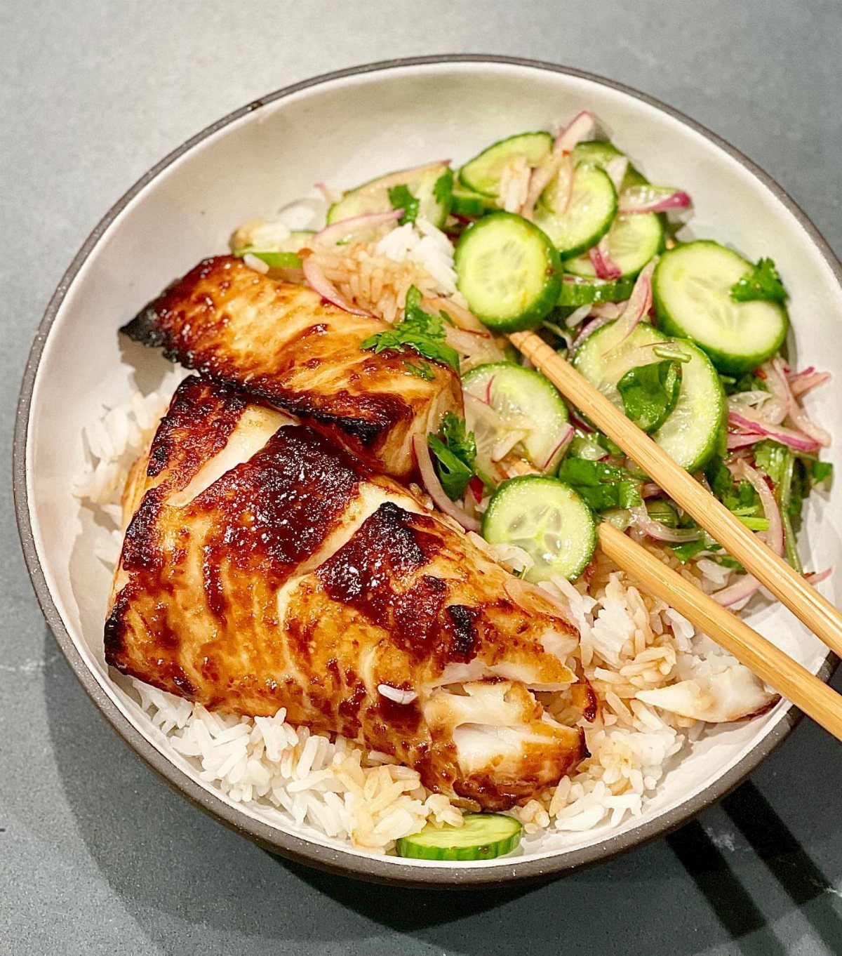 Glazed salmon fillets served with white rice and a cucumber onion salad.