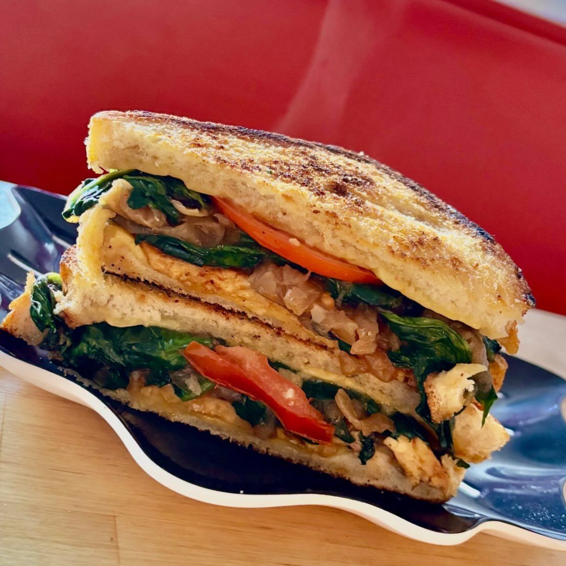 Grilled cheese sandwich with spinach, caramelized onions, and tomato on a black plate.