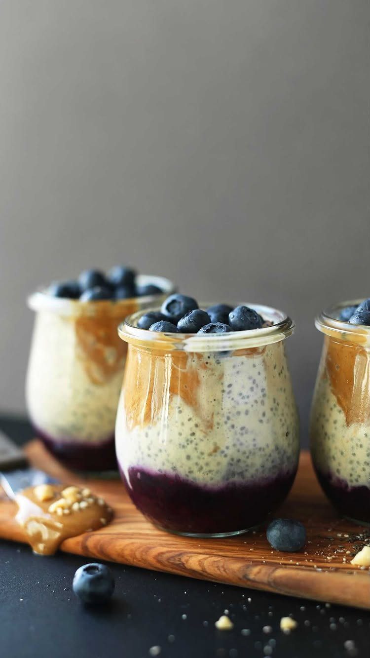 Layered chia pudding in glass jars topped with fresh blueberries on wooden board