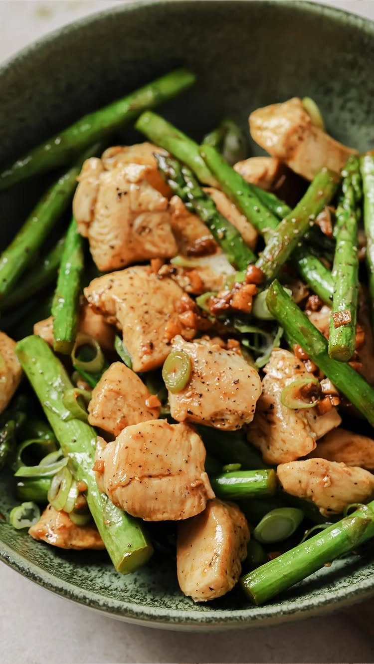 Chicken chunks and asparagus spears seasoned with garlic in a green bowl.